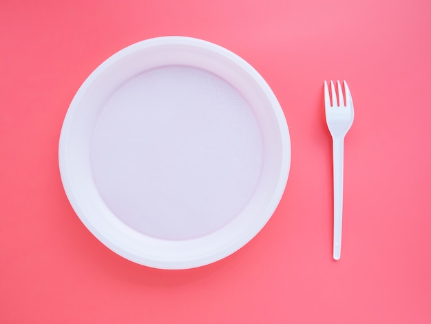 White plastic plate and fork on pink background