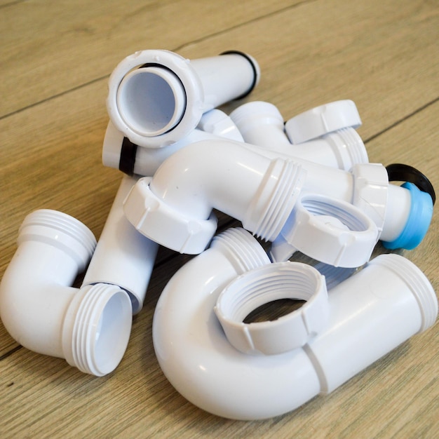Белые пластиковые сантехнические трубы, гладкие и изогнутые фитинги, фланцы, резиновые прокладки.