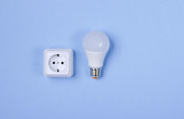 White plastic power socket and LED light bulb on purple background. Minimalism. Top view