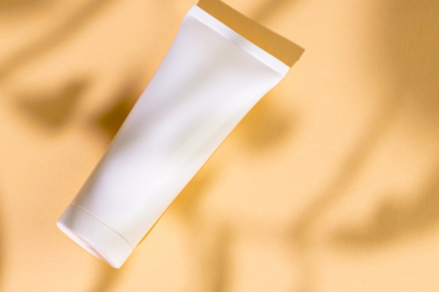 White plastic skincare tubes on a background of tropical plant shadow with copy space