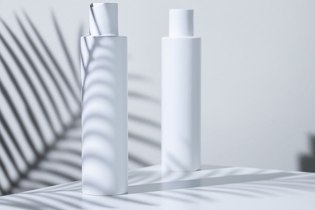 White plastic skincare tubes on a background of tropical plant shadow with copy space