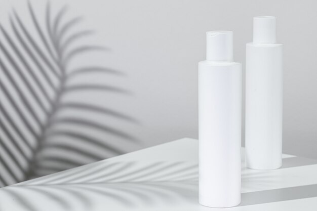 White plastic skincare tubes with tropical plant shadow