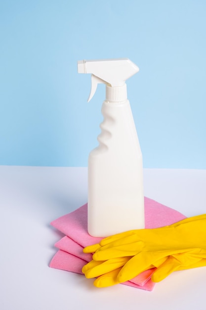 White plastic spray bottle and yellow rubber protective glove on a rag on blue background