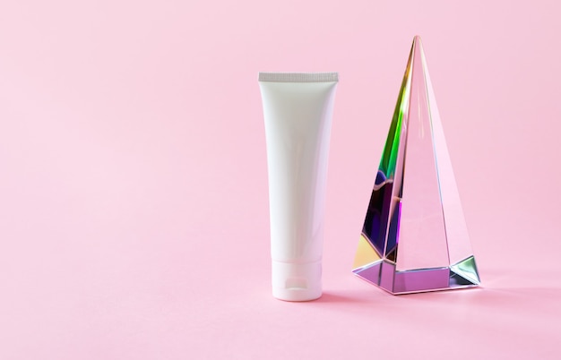 Photo white plastic tube mockup with moisturizer cream shampoo or facial cleanser and glass pyramid prism