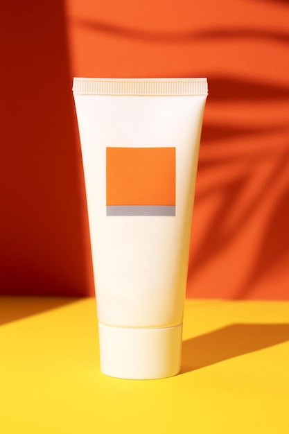 White plastic tube with face hand and body cream on an orange background with palm leaves shadow Sun protection lotion sunscreen Summer skin care concept with spf Mockup