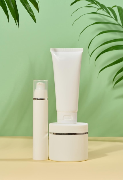 White plastic tubes jars on a green background containers for cosmetic creams and gels