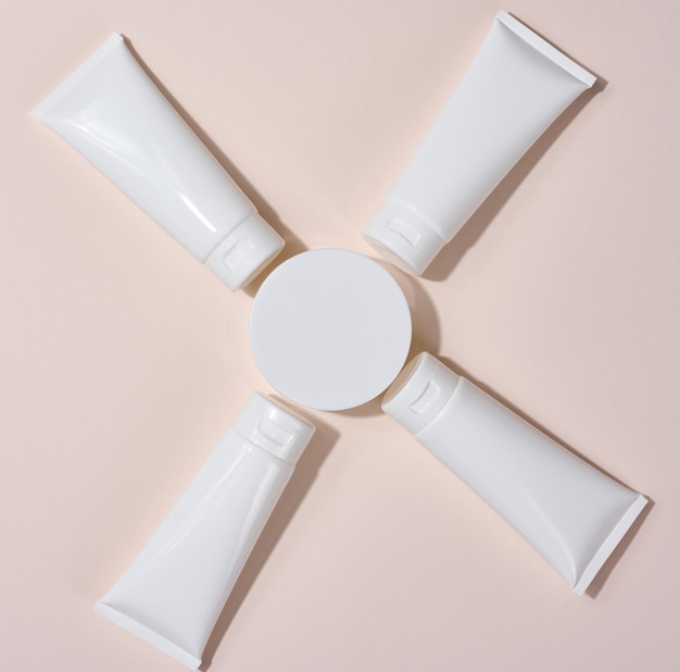 White plastic tubes jars and other form of packaging for cosmetics on a beige background top view Template for branding advertising and product promotion