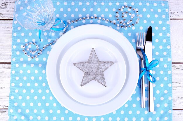 White plate, fork, knife and Christmas decoration on polka dot napkin on wooden table