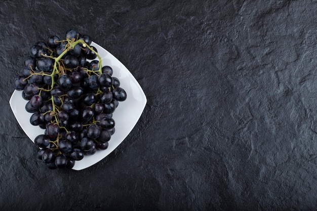 White plate of fresh black grapes on black surface