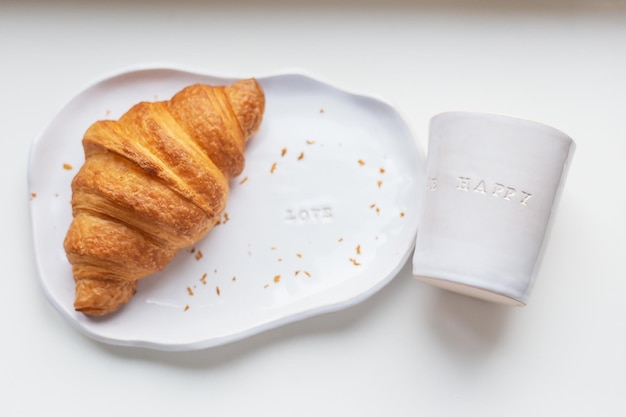 White plate and glass made of handmade clay with fresh croissant on a white table
