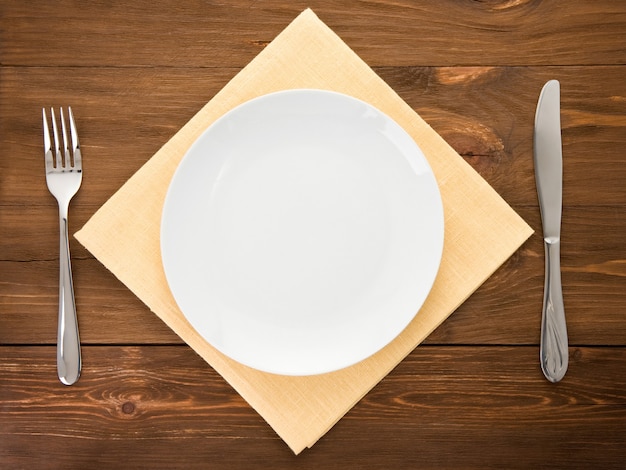 White plate, knife and fork at napkin on wooden 