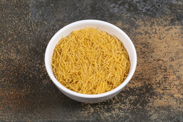 White plate of raw dry spaghetti on marble surface.