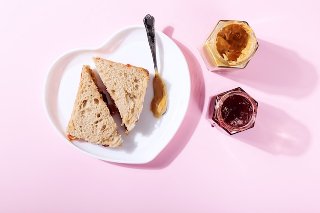 White plate in shape of heart with sandwiches with peanut butter and strawberry jelly on pink