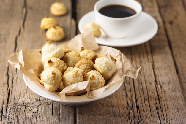 White Plate of Sweet Coconut Cookies and White Cup of Coffee on Old Wooden Background Horizontal