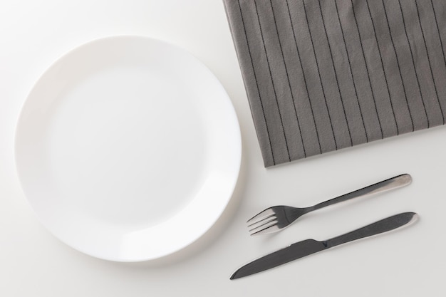 A white plate on a white table with cutlery placed There is no food on the plate. Household equipment