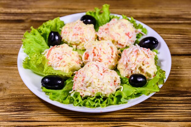 White plate with crabcheese balls black olives and lettuce leaves on rustic wooden table