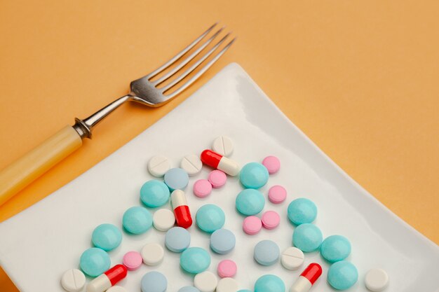 White plate with different pills on it with knife and fork concept of drugs addiction