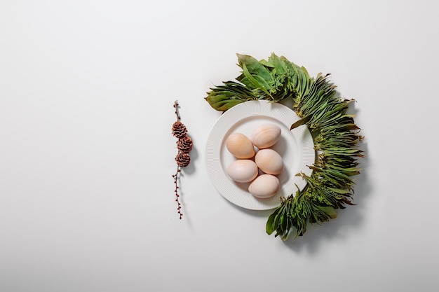 White plate with eggs and green leaves on white background