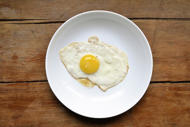 White plate with fresh fried egg on the vintage wooden table