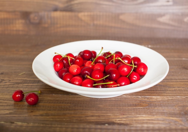 Белая тарелка со свежими красными вишнями на коричневом деревянном столе