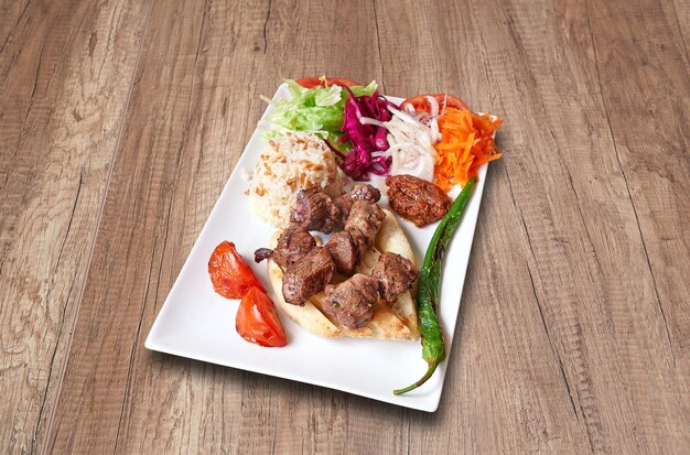 White plate with Lamb Kebab and vegetables on wooden table