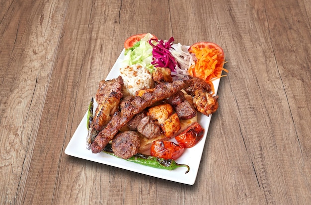 White plate with mixed meats and vegetables on wooden table