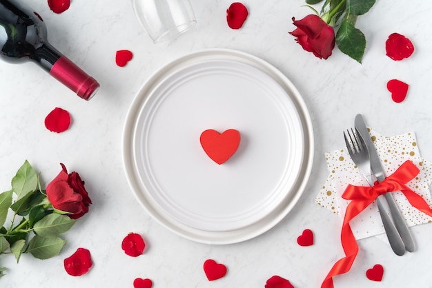 White plate with red rose flower on marble white table background for Valentine's Day dating holiday meal concept.