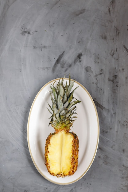 Foto piastra bianca con ananas a fette mature su sfondo grigio cemento. copyspace.