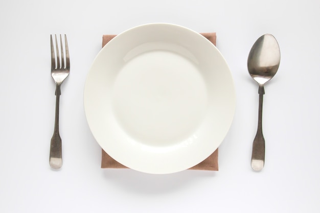 Photo a white plate with silver fork and spoon isolated on white background.