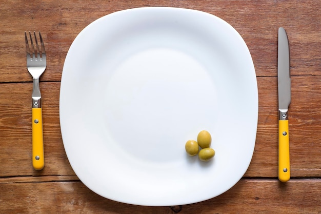 White plate with three olives and cutlery on vintage wooden table