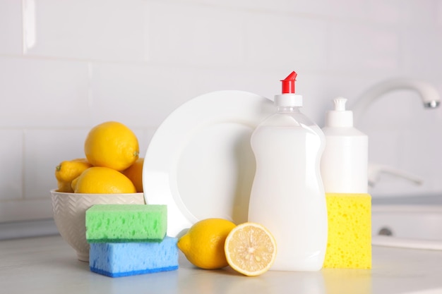 A white plate with a yellow sponge, a white dish with a blue container of lemons, a white dish with a lemon on it.