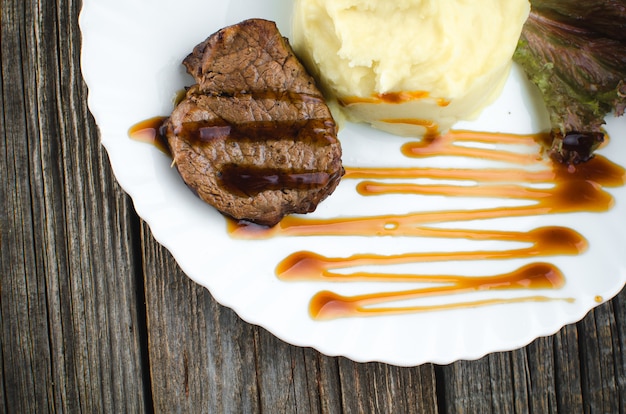 On a white plate, on a wooden background, mashed potatoes with beef meat beautifully polished balsamic sauce