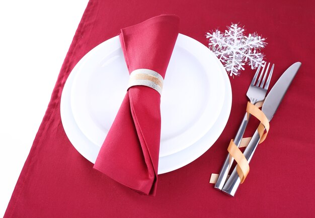 White plates, fork, knife and napkin on burgundy tablecloth isolated on white