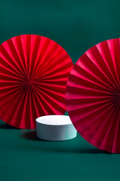 緑の背景に装飾的な赤い扇子と白い表彰台または台座。製品プレゼンテーションのコンセプト。コピースペース付き。垂直フォーマット
