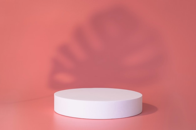 White podium on the pink background with leaves shadows. Podium for product, cosmetic presentation. Creative mock up. Pedestal or platform for beauty products. Minimalist design.