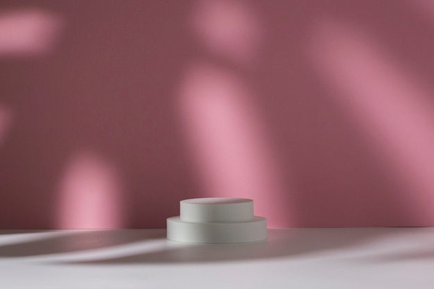 Photo white podiums for presentation and shadow of monstera leaf on white pink background.