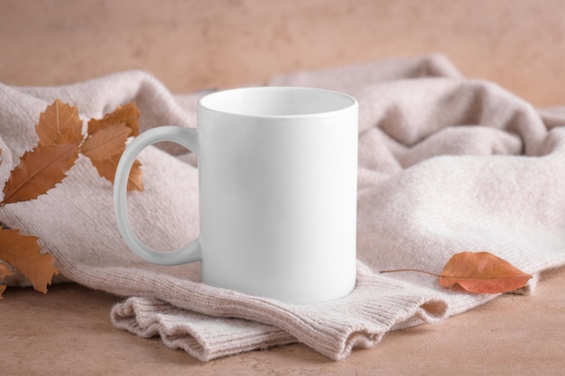 White porcelain coffee mug mockup on beige stone table with beige sweater and dry fall leaves