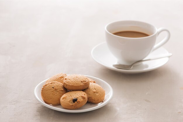 white porcelain cup of coffee with biscuits, spoon and plate on light background