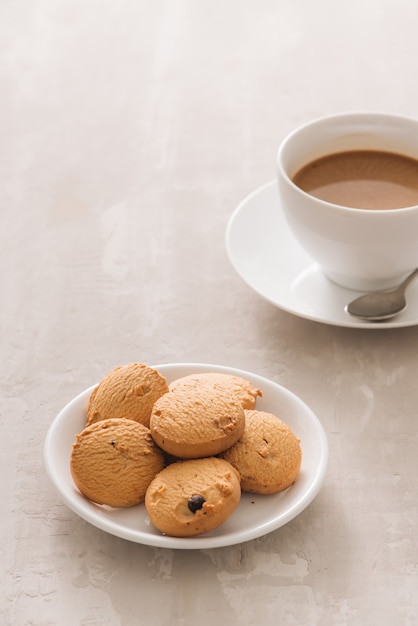 white porcelain cup of coffee with biscuits, spoon and plate on light background