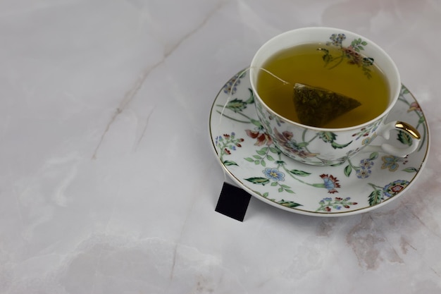 White porcelain cup on a saucer with a brewing green tea bag on a white marble table