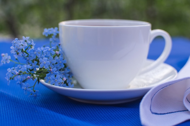 White porcelain cup with tea on the table with blue tablecloth and white napkin