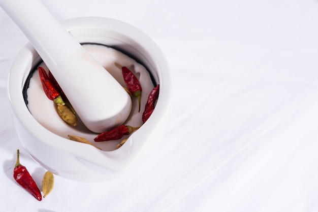 White porcelain mortar and pestle with chili peppers and cardamom isolated on textile table, copy space