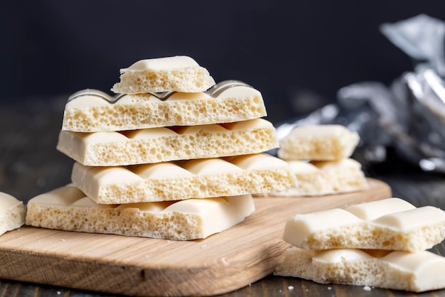 White porous chocolate on a wooden table, pieces of white\
porous chocolate in packaging foil