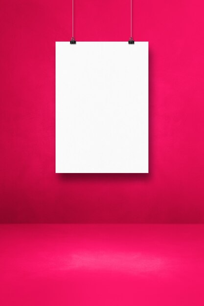 Foto poster bianco appeso a una parete rosa con clip. modello di mockup vuoto