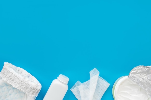 White powder, diaper, cream, napkin on a blue background, flatley, top view, copy space, mock up. Baby hygiene, background for newborn boys.