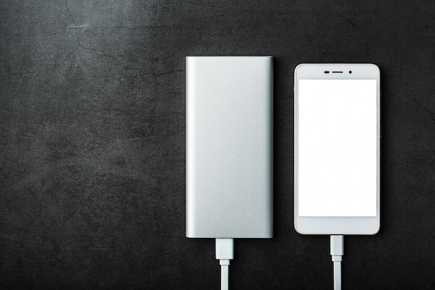 A white Powerbank charges a smartphone . Universal external battery for gadgets Free space.