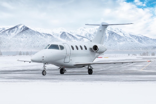 White private jet taxiing on airport taxiway in winter on the background of snow capped mountains