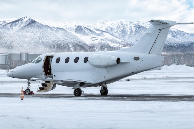 Белый частный самолет с открытой дверью трапа на фоне высоких живописных заснеженных гор