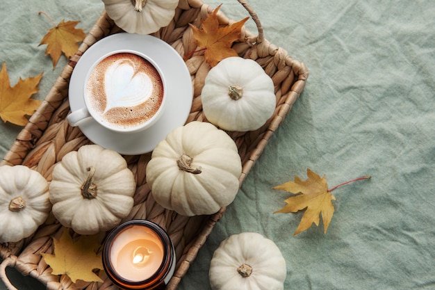 White pumpkins coffee and autumn leaves on a wicker tray