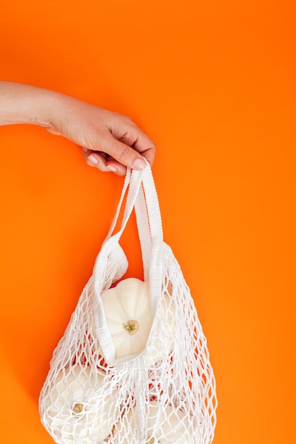 White pumpkins in mesh shopping bag on orange background